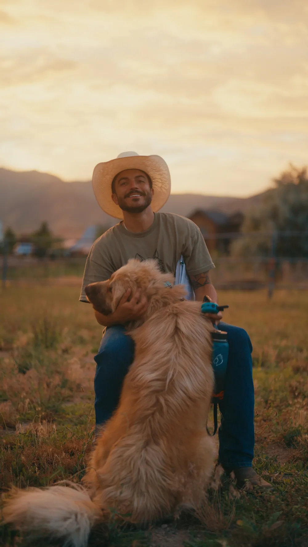 A rancher in a cowboy hat with his golden retriever at sunset.